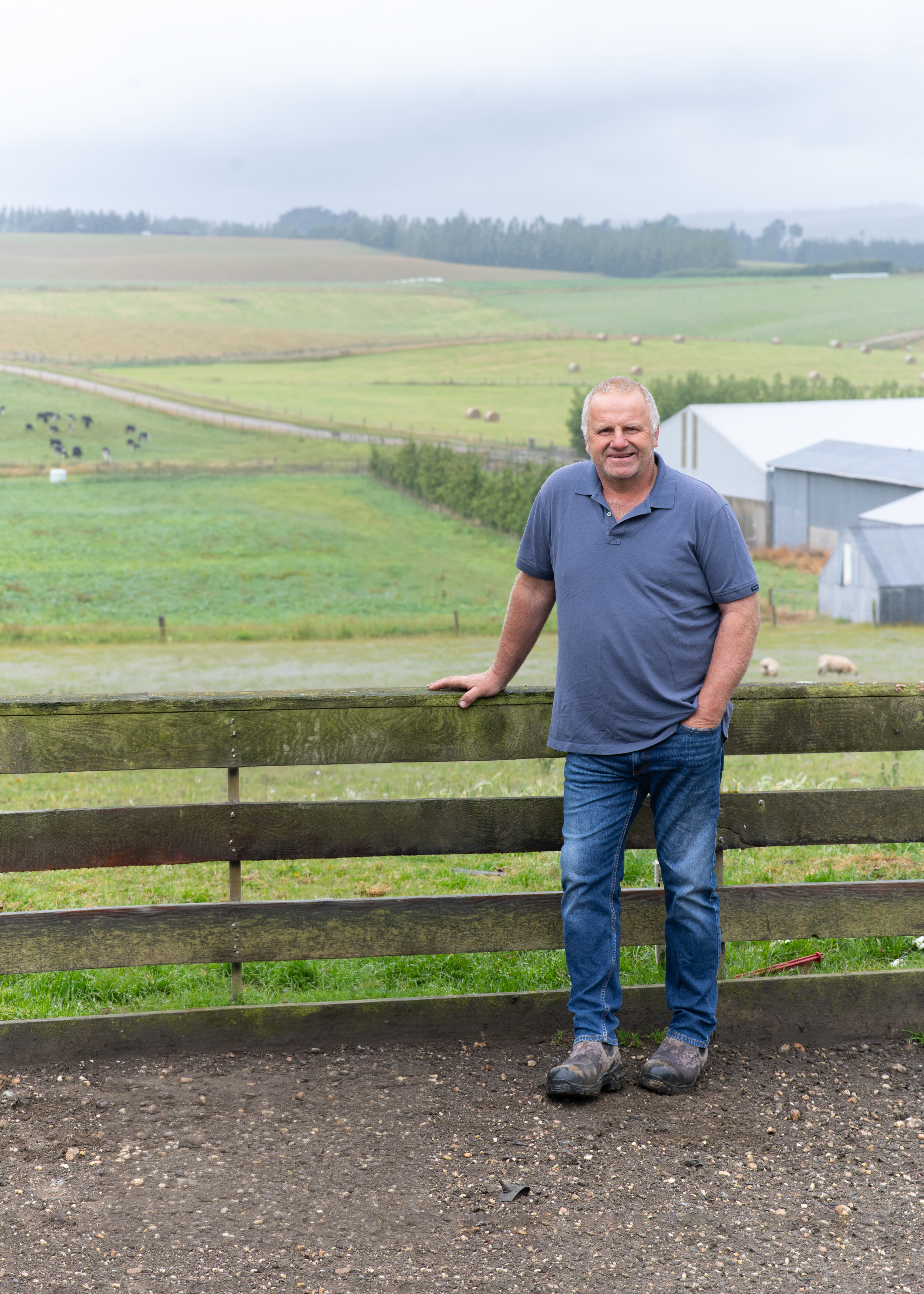 Environment Southland Chair Jeremy McPhail​ leaning on a wooden fence in Waikaka Valley with farmland in the background.