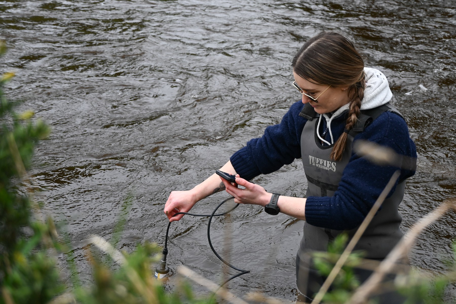 A woman standing in a river taking a water sample
